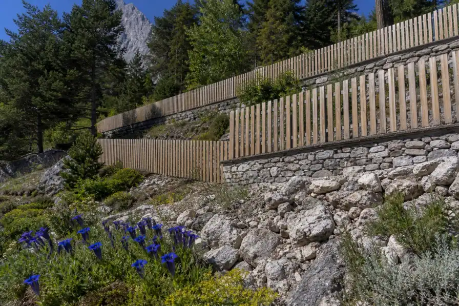 Clôture bois suivant une restanque en escalier sur un coteau au-dessus de Gap, chaque tronçon calé de niveau, jardin de rocaille et gentiane au premier plan.
