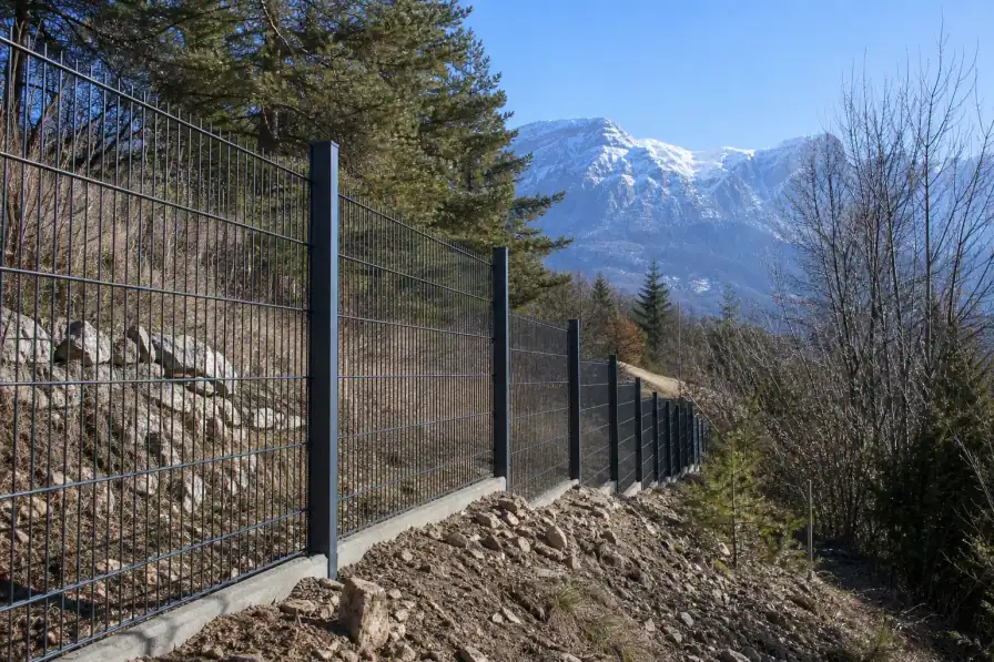 Clôture en panneaux rigides fraîchement posée le long d'un terrain en pente à la sortie de Gap, poteaux alignés au cordeau, sommets enneigés du Dévoluy en arrière-plan, lumière vive d'altitude, aucune personne visible.