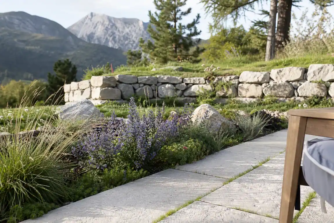Jonction terrasse-jardin finie : bordure plantée de vivaces rustiques et joint engazonné au pied des dalles, restanque de pierre en arrière-plan.